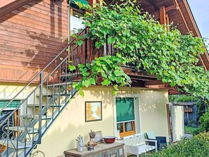 A wooden house with a balcony covered in green vines, a staircase, and outdoor furniture. - Wörtherseenahe Ferienwohnung im Grünen by Interhome (Schiefling am See)