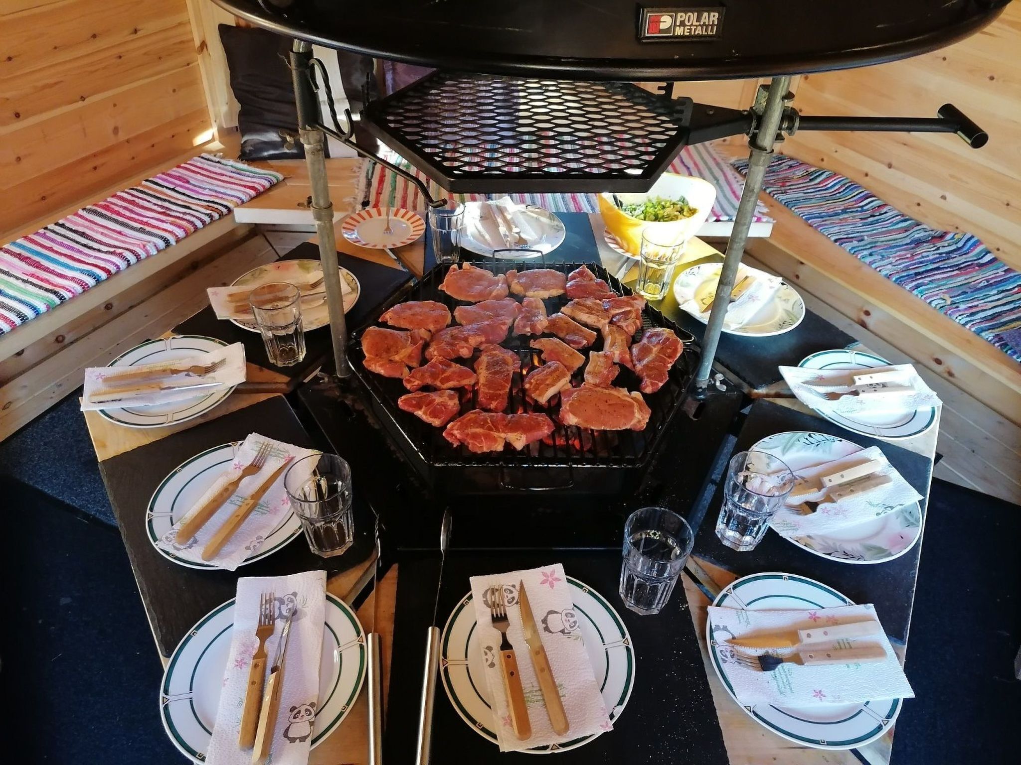 Un comedor con una parrilla, varios platos, cubiertos y vasos dispuestos alrededor de una mesa central.