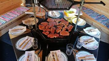 Un comedor con una parrilla, varios platos, cubiertos y vasos dispuestos alrededor de una mesa central.