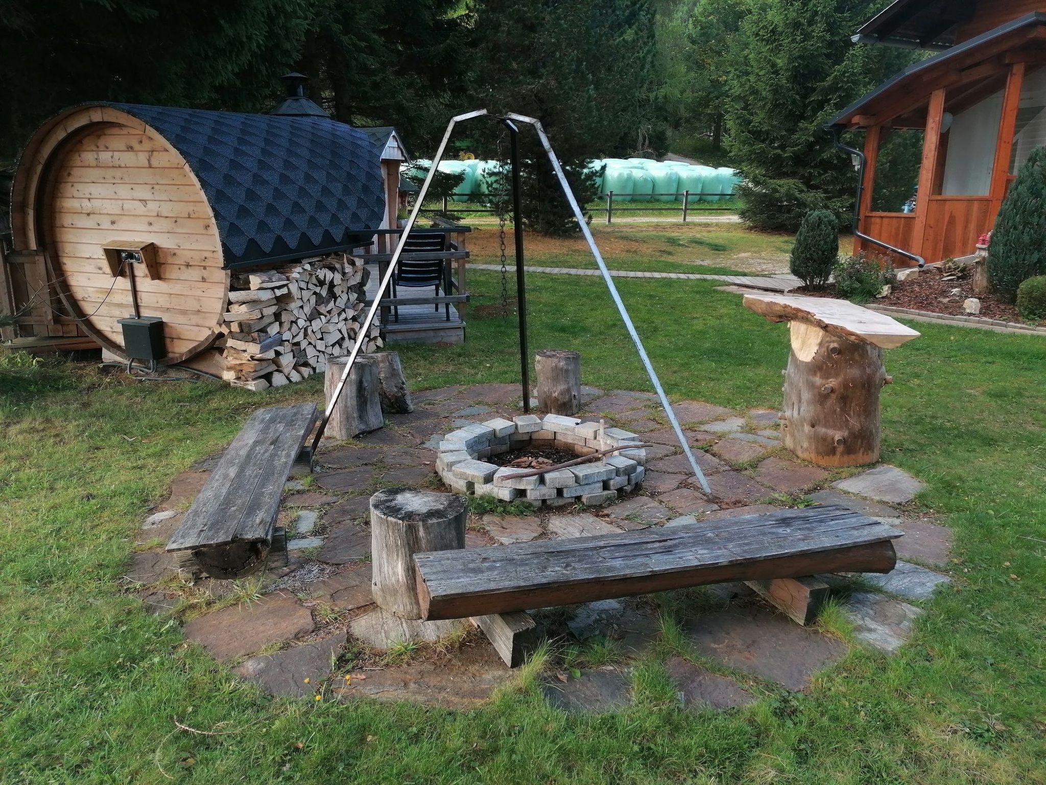 Een rustieke buitenruimte met een houten constructie, een vuurkorf en een schommel.