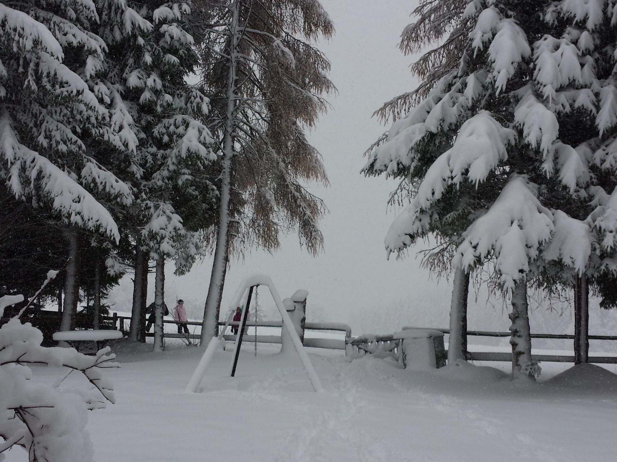 Un parque cubierto de nieve con un columpio y bancos.