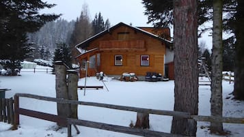 Eine Holzhütte mit einem Balkon, umgeben von schneebedecktem Gelände und Bäumen.