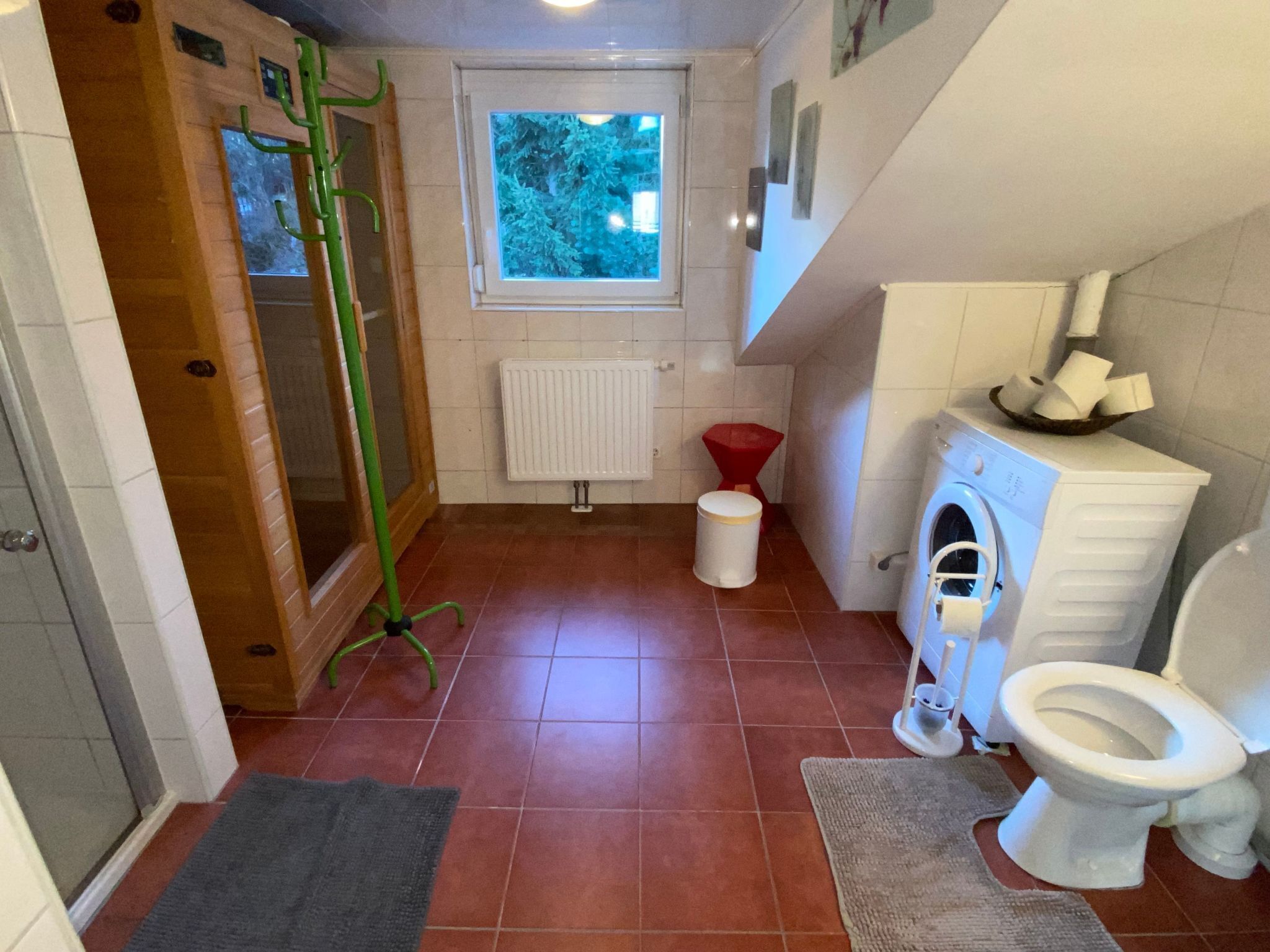 Un baño pequeño con inodoro, lavadora, radiador y ventana que proporciona luz natural.