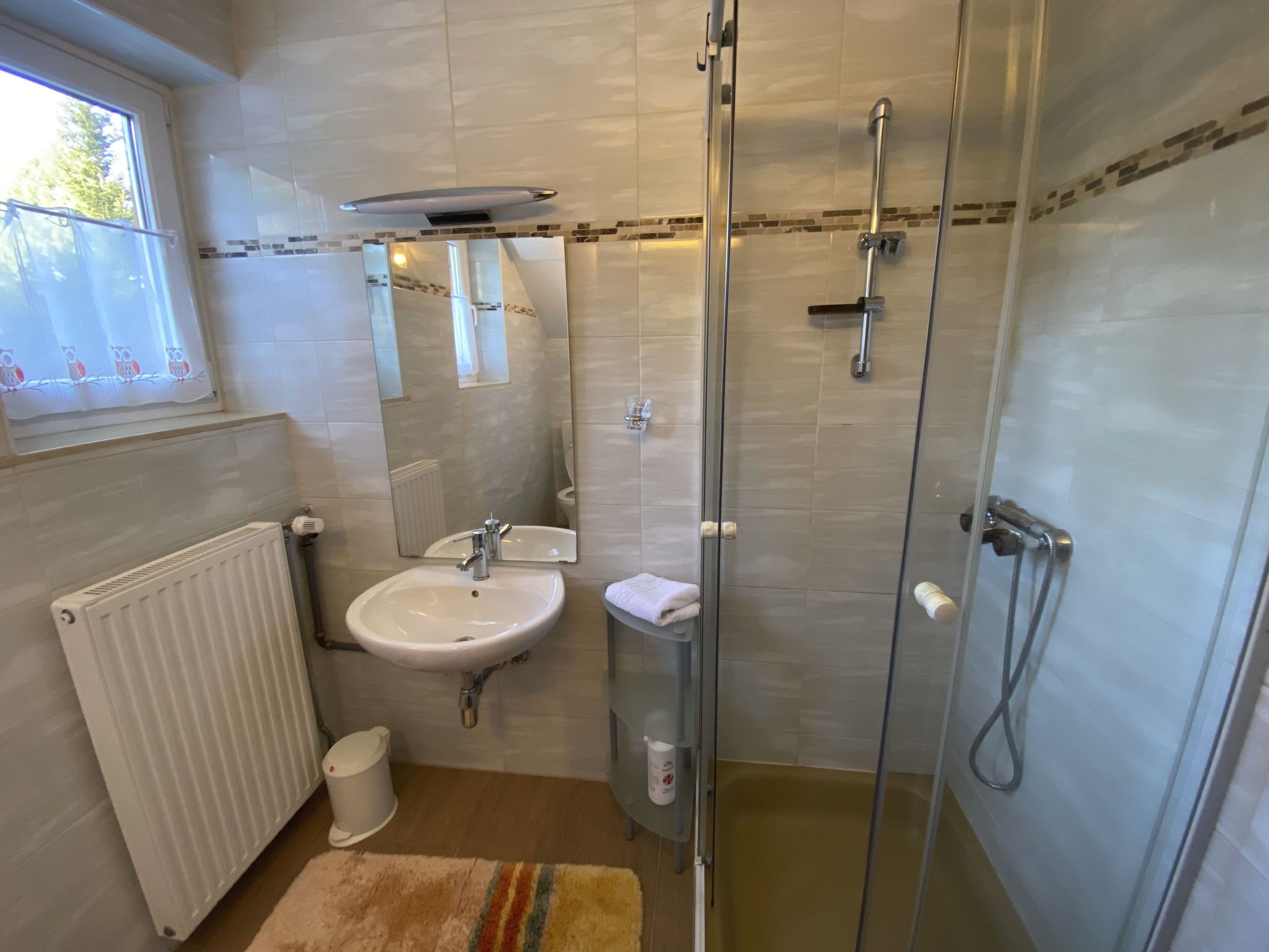 Ein modernes Badezimmer mit einer Duschkabine aus Glas, einem weißen Waschbecken und einem Fenster mit einer Eulen-Vorhang.