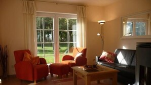 A living room with a red armchair, a sofa, a coffee table, and a TV. There are large windows with curtains, and a lamp is visible. - Kliffkieker by Interhome (Ahlbeck)