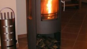 A wood-burning stove with a visible fire, a metal ashtray, and a staircase in the background. - Kliffkieker by Interhome (Ahlbeck)