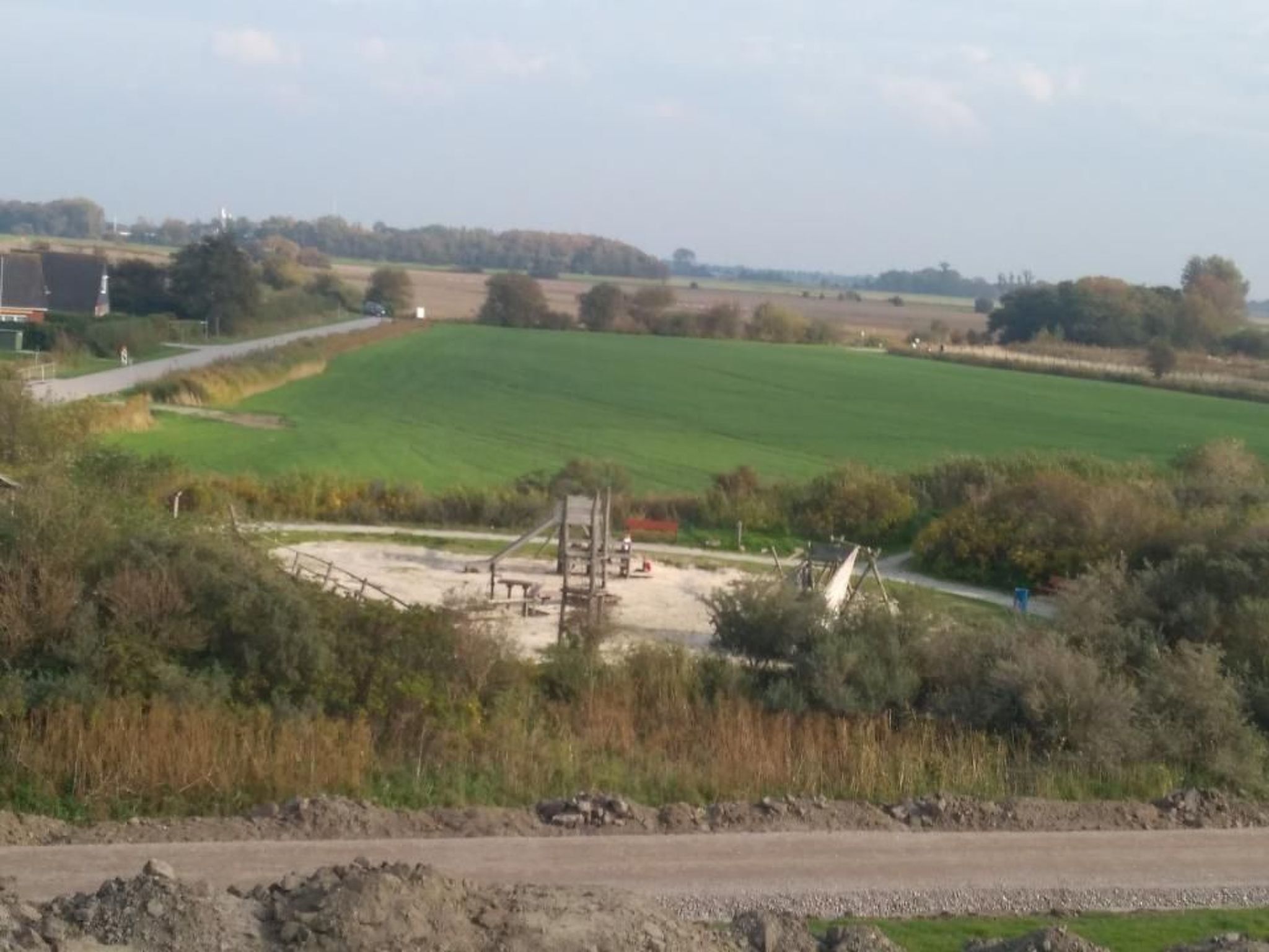 Un paisaje rural con un extenso campo verde, un camino de tierra y algunos equipos de construcción.