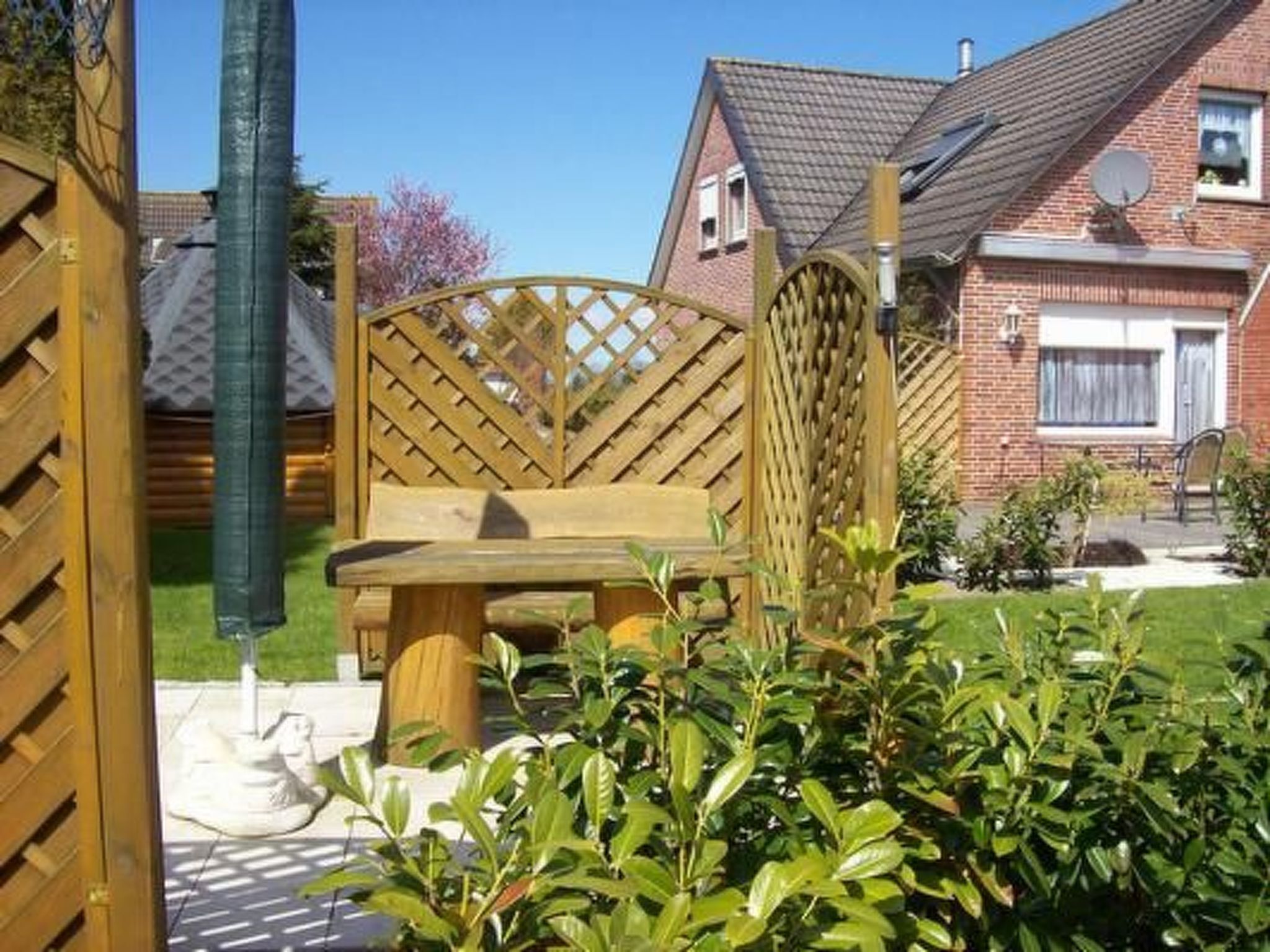 A wooden bench in a garden with a brick house in the background.