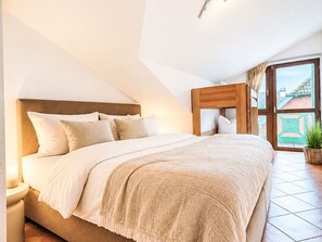 A bedroom with a large bed, a wooden headboard, a nightstand, a potted plant, and a view of the outside through a glass door. - Zeesenhaus 6 by Interhome (Ostseebad Sellin)