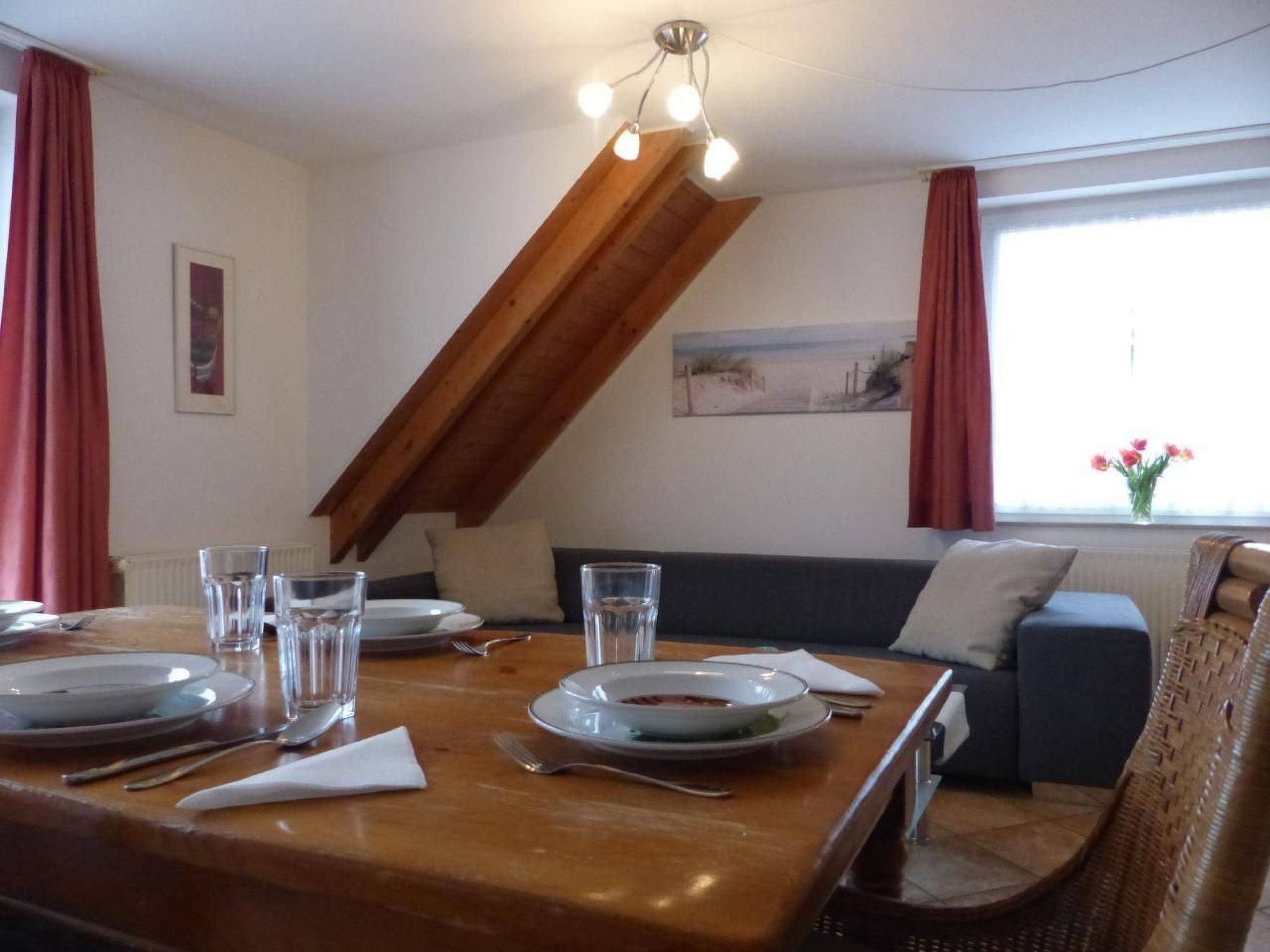 Ein Essbereich mit einem Holztisch, gedeckt für zwei Personen, einer Couch und einem Bild an der Wand.