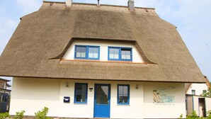 Een traditioneel huis met rieten dak, een blauwe deur en een kleine tuin met rotsen en struiken.