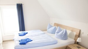 Een eenpersoonsbed met houten hoofdbord, een nachtkastje met lamp en een raam met gordijnen.