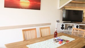 Een eetgedeelte met een houten tafel, stoelen, een televisie en een schilderij van een ondergaande zon.