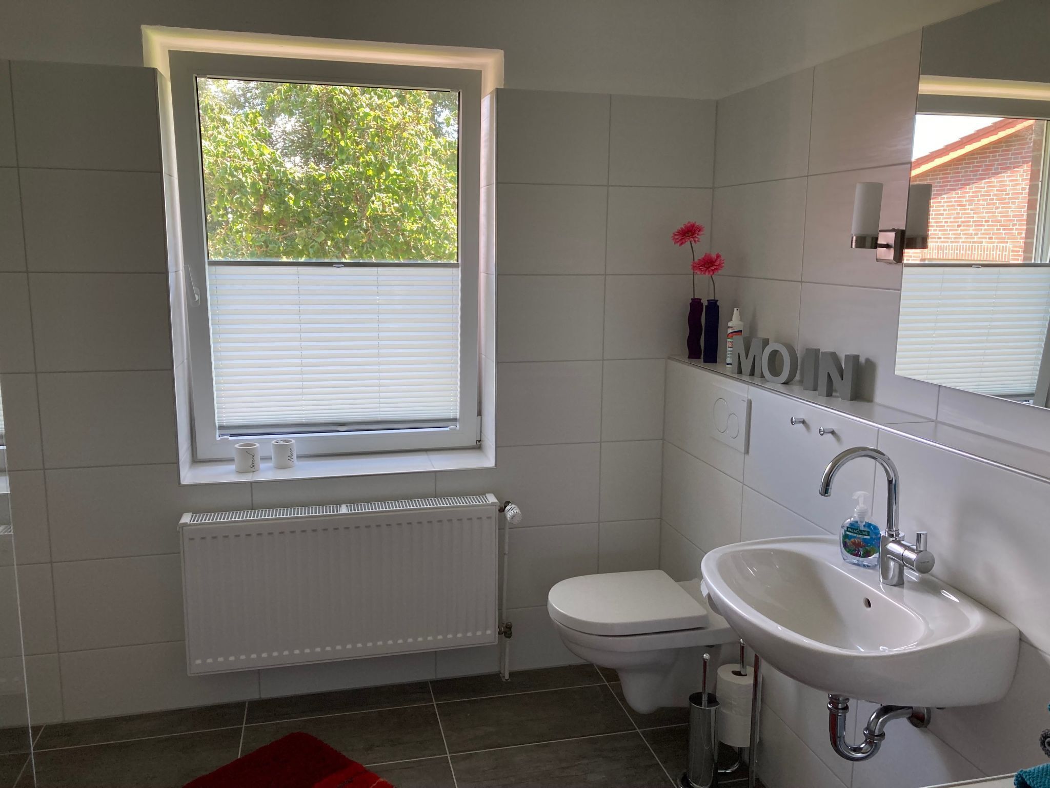 A modern bathroom with a window, white tiles, a toilet, a sink, and a radiator.