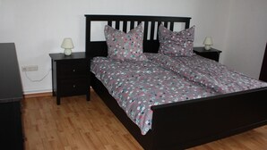 Une chambre à coucher avec un lit en bois, deux tables de chevet, une lampe sur chacune, et une prise électrique au mur.