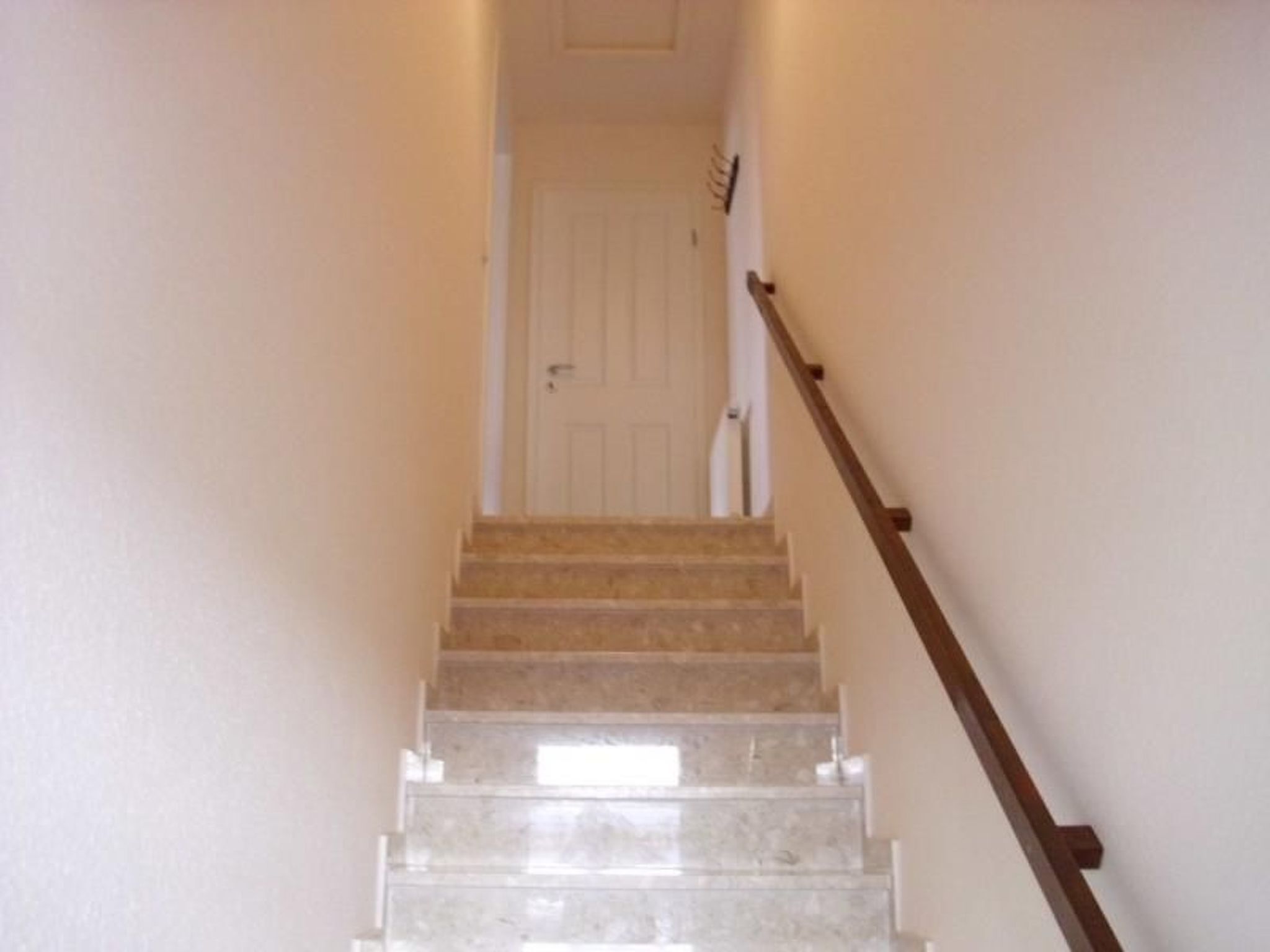 Una escalera con barandilla de madera que lleva a una puerta blanca al final.