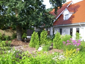 Ett vitt hus med ett rött tak, omgivet av en trädgård med olika växter och blommor.