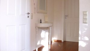 A hallway with a white door, a white wall-mounted mirror, and a small white pedestal table with a sink. - Wohnung in Abbehausen - Ellwürden by Interhome (Abbehausen)