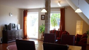 A living room with a dining area, a television on a cabinet, and a large window with curtains. - Wohnung in Abbehausen - Ellwürden by Interhome (Abbehausen)