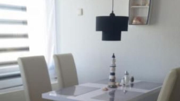 Un comedor con una mesa y sillas blancas, una lámpara colgante negra y un pequeño objeto decorativo sobre la mesa.