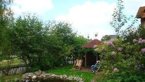 Ein Garten mit Teich, Holzzaun und einem Pavillon, in dem eine Person sitzt.