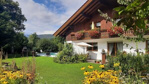 Una casa de madera con balcón, piscina y un jardín bien cuidado con flores amarillas.