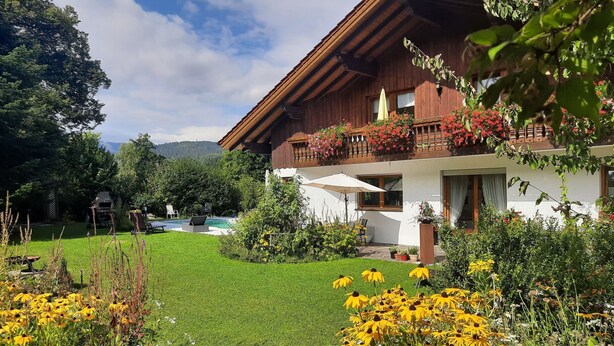 Ein Holzhaus mit Balkon, Schwimmbad und einem gepflegten Garten mit gelben Blumen.