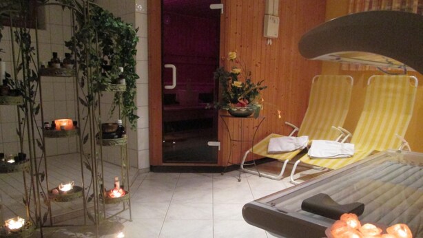 Un cuarto de spa con una camilla de masaje, dos sillones de descanso, una mesita con velas y un arreglo de plantas.