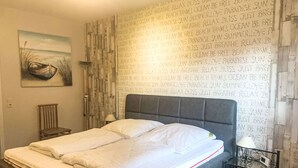 Ein ordentlich bezogenes Bett mit weißer Bettwäsche in einem Zimmer mit Wandtapete mit Muster und einem Gemälde eines Bootes an der Wand.