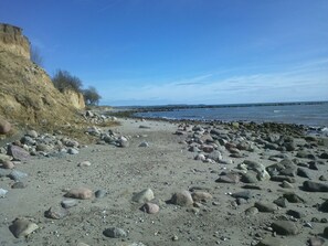 A rocky beach with a cliff on the left and calm water in the background. - Familienfreundliche Ferienwohnung auf Fehmarn by Interhome (Bannesdorf)