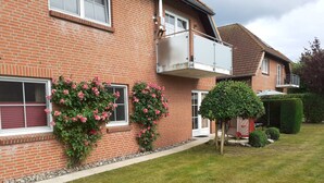 Ein zweistöckiges Ziegelhaus mit Balkon, einem kleinen Garten mit rosa Rosen und einer ordentlich gestutzten Hecke.
