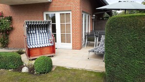 Eine Terrasse mit einem rot-ziegelbau, einem überdachten Sitzbereich mit gestreiften Kissen und einem ordentlich geschnittenen Heckenstreifen.