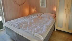 Ein Schlafzimmer mit Holzboden, einem Bett mit weißer Bettwäsche, einer Wanduhr und einem Kleiderschrank mit Glastüren.