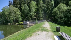 A gravel path beside a calm lake, a wooden bench, and a stone bridge. - Gretelhaus by Interhome (Auerbach)
