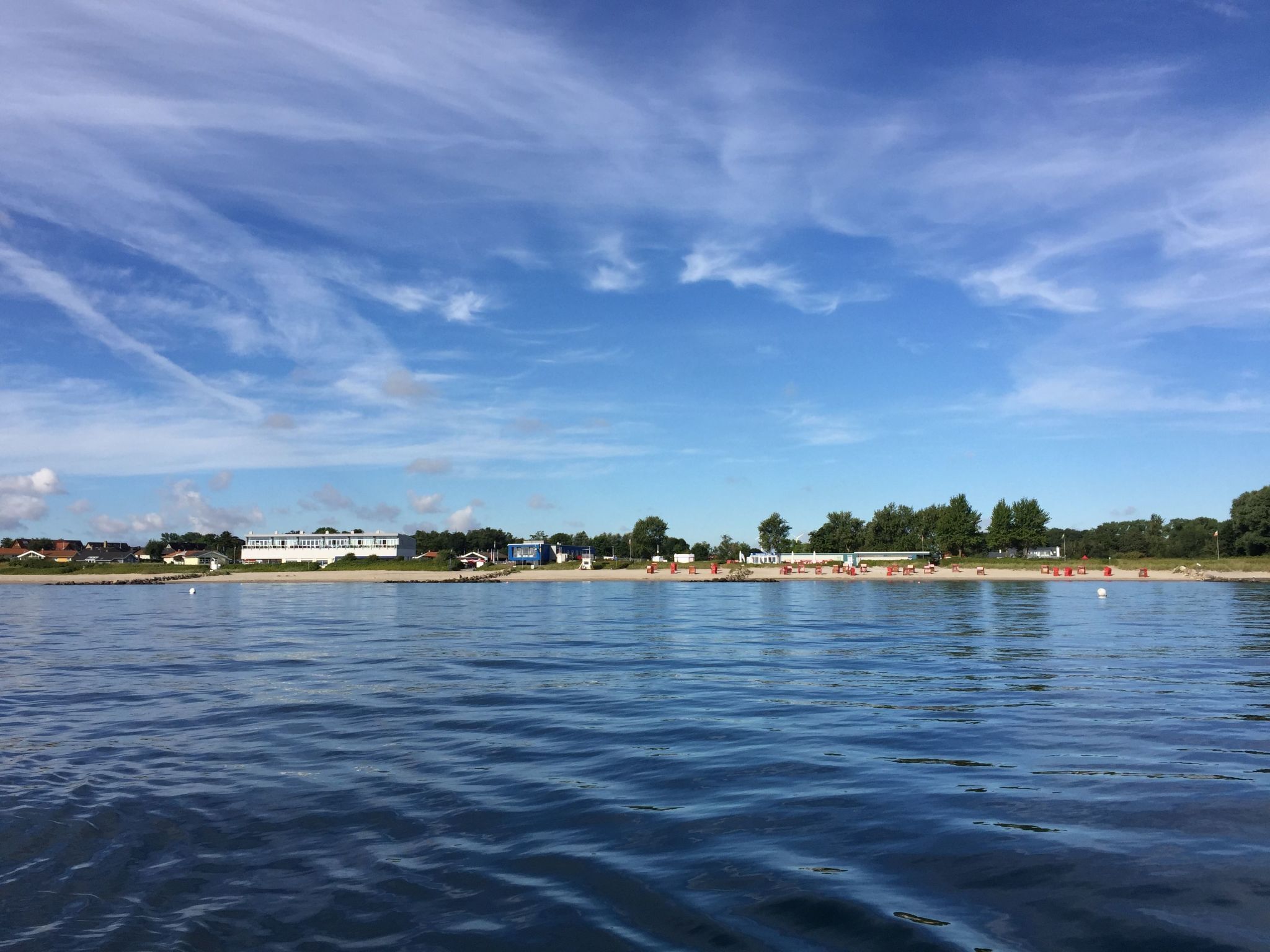 Una spiaggia con un mare calmo, cielo sereno e edifici sullo sfondo.