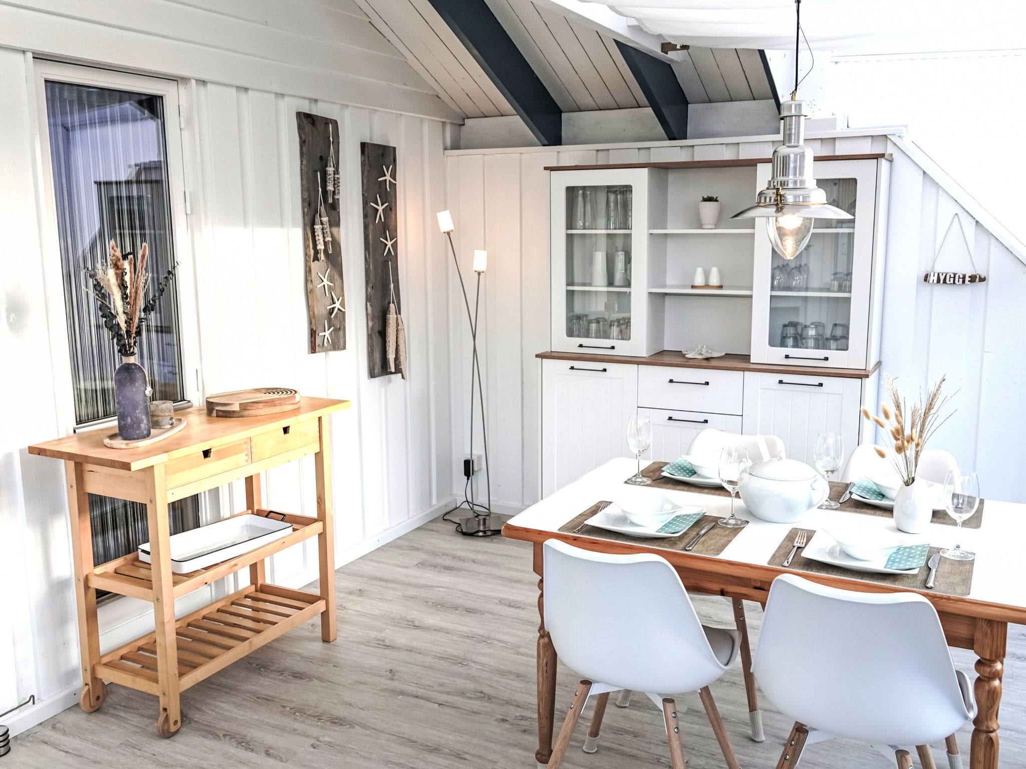 A modern kitchen with white cabinetry, a wooden dining table set for four, and a pendant light above the table.