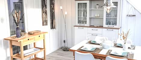 Ett modernt kök med vita köksskåp, ett träbord med plats för fyra personer och en hänglampa ovanför bordet.