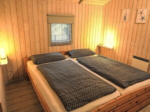 A wooden-paneled room with a bed, two bedside lamps, a window with a curtain, and wall decorations. - hygge hus, tolle Ostseelage, freier Blick auf Felder by Interhome (Brodersby)