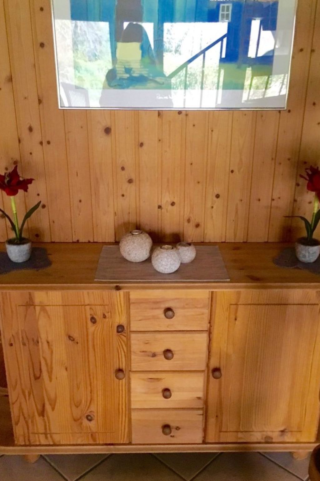 A wooden cabin-style room with a wooden dresser, a mirror, and two potted red flowers.