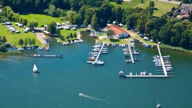 An aerial view of a marina with boats docked, surrounded by greenery and residential buildings. - Uferpromenade 1 EG by Interhome (Waren)
