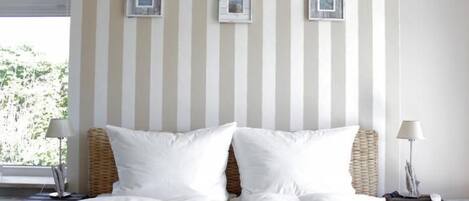 Een hotelkamer met een groot bed, gestreepte behang en drie kleine afbeeldingen in lijsten aan de muur.