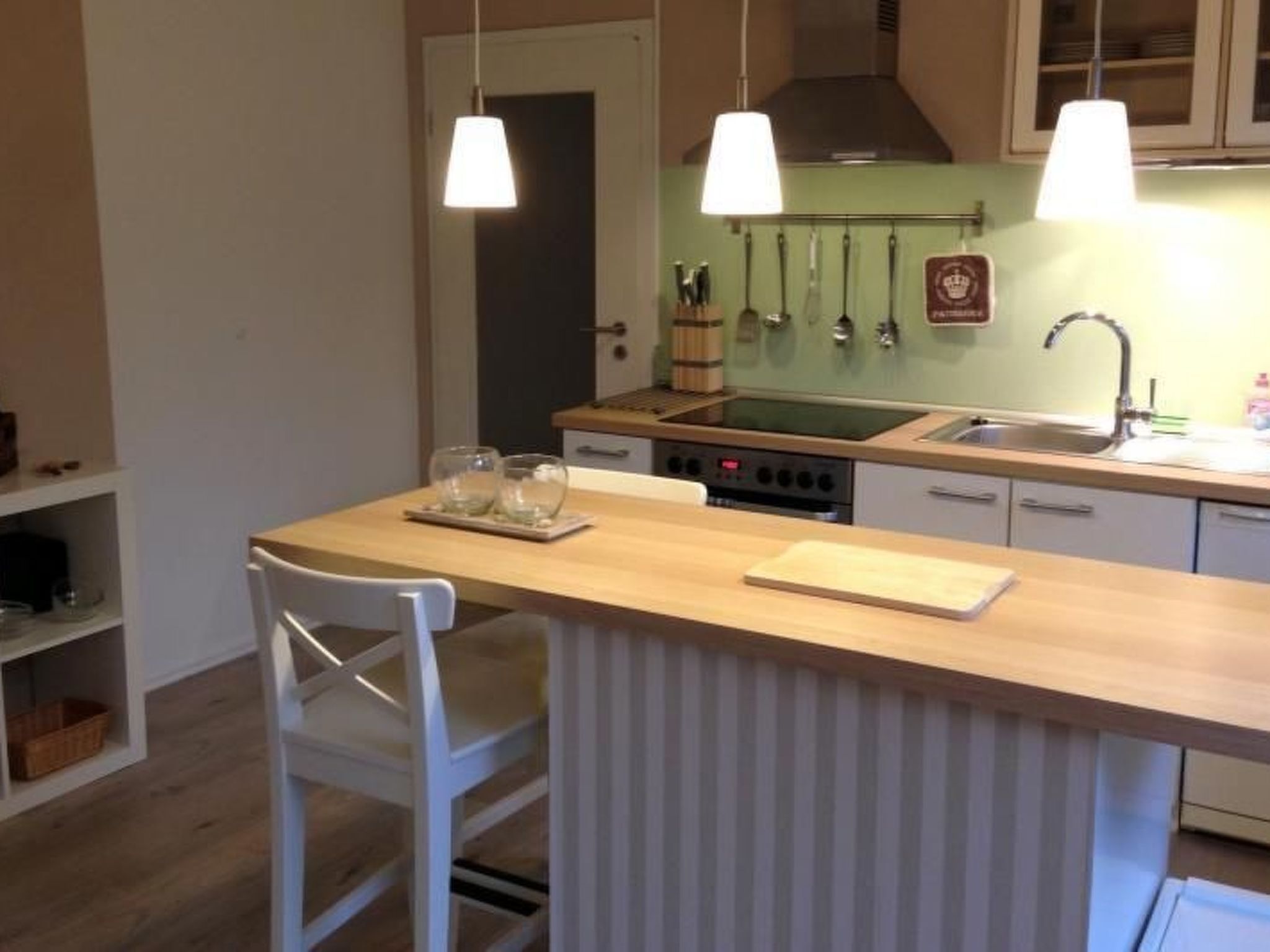 A kitchen with a central island, a stove, and a sink. There are hanging lights above the island and a window with a view of the outside.