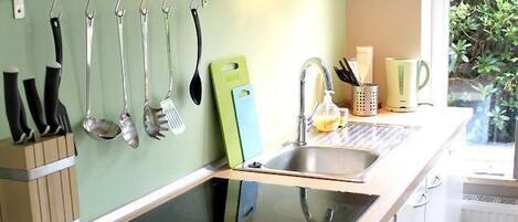 A modern kitchen with a built-in stove, a hanging utensil rack, a sink, and a window with a view of greenery.