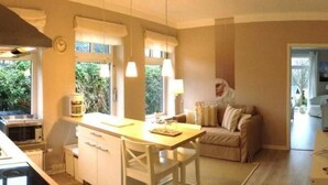 Een moderne keuken met een houten tafel en witte kasten, een zithoek met een bank, en uitzicht op groen.