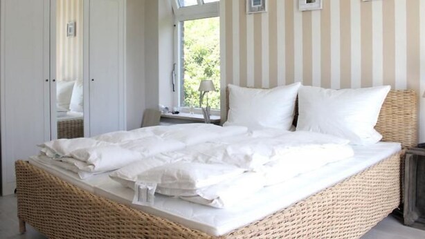 Een slaapkamer met een rieten bed, een kledingkast en een raam met gordijnen.