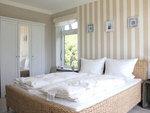 Ein Schlafzimmer mit einem Korbmöbelbett, einem Kleiderschrank und einem Fenster mit Vorhängen.