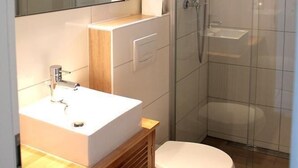 Een moderne badkamer met een douchecabine van glas, een witte wastafel en een grote spiegel.