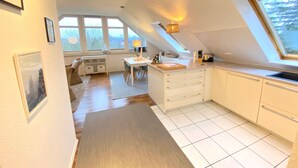 Une cuisine moderne avec des meubles blancs, un coin repas comprenant une table et des chaises, et de grandes fenêtres laissant entrer la lumière naturelle.