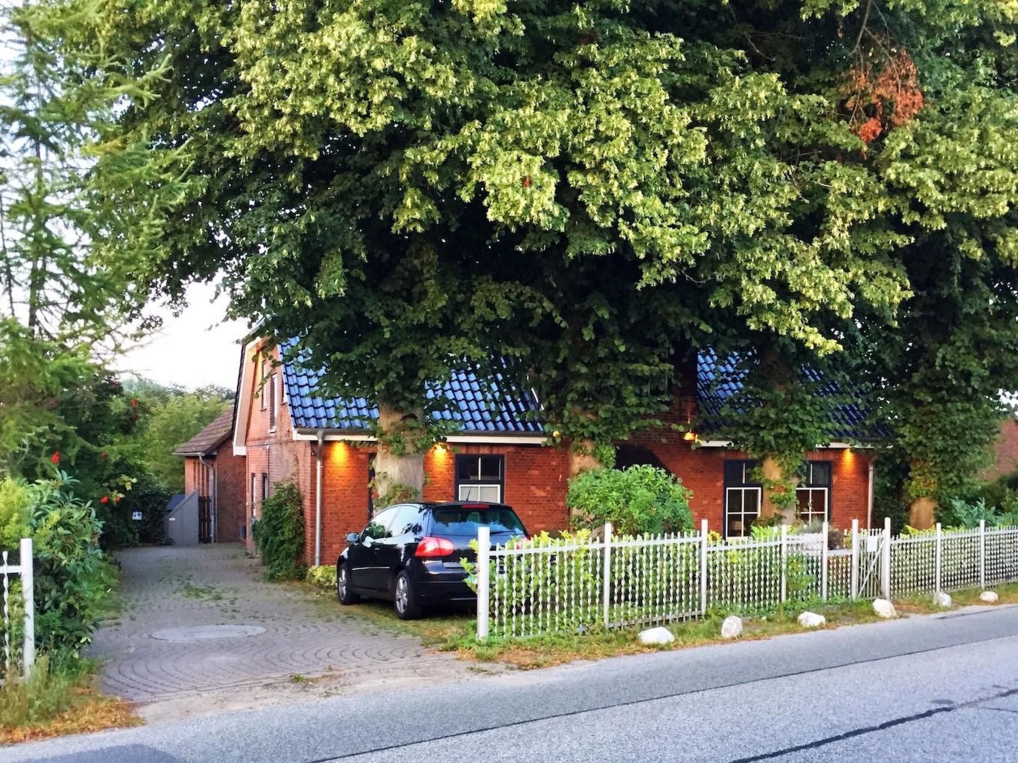 Ein Ziegelhaus mit Ziegeldach, ein geparktes Auto davor und ein weißer Zaun.
