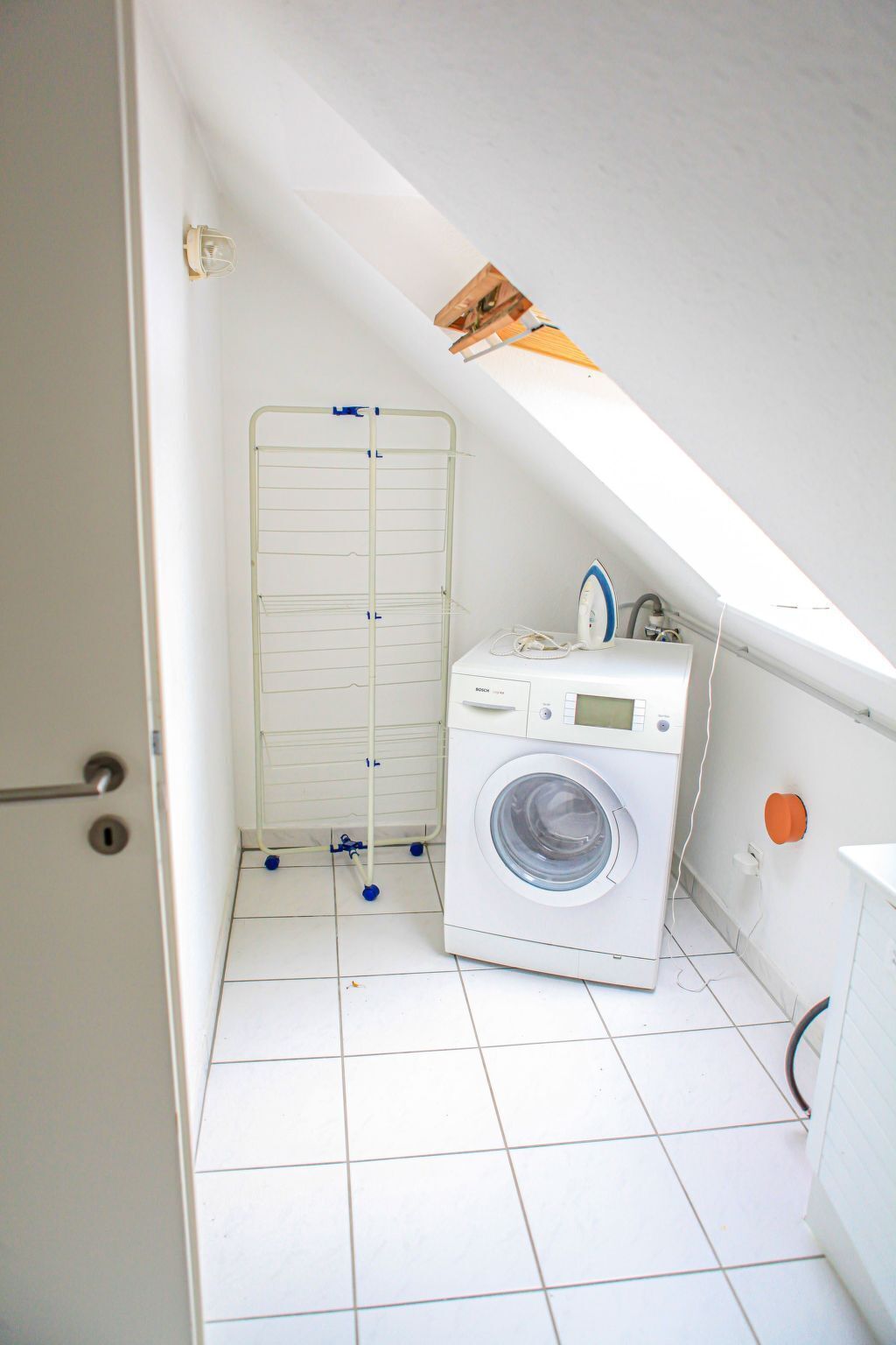 A small laundry room with a Bosch washing machine, a drying rack, and a skylight.